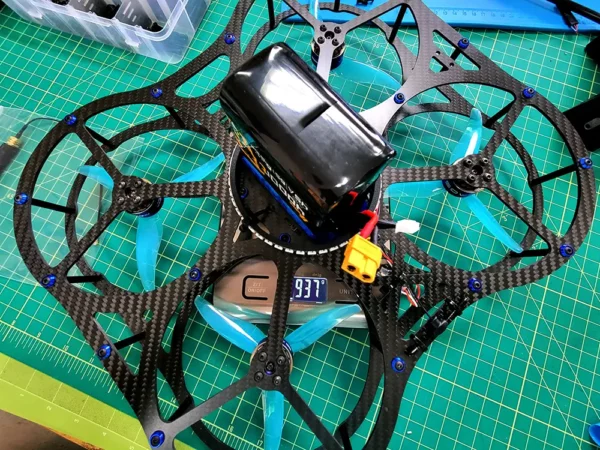 Close-up of a custom-built drone with a carbon fiber frame and blue LED lights, placed on a green cutting mat.