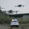 Two drones flying above a police car with flashing lights in an outdoor setting
