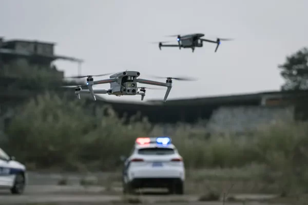 Two drones flying above a police car with flashing lights in an outdoor setting