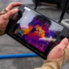 Close-up of hands operating a drone controller with a thermal imaging display.
