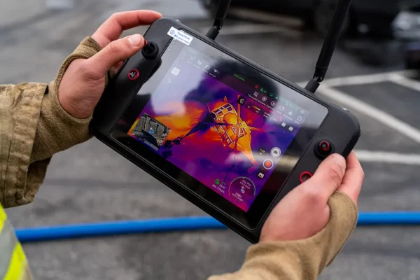 Close-up of hands operating a drone controller with a thermal imaging display.