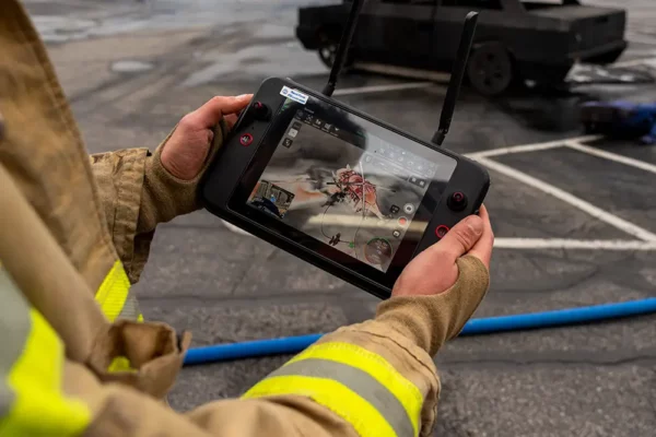 Firefighter holding a drone controller with a live thermal imaging feed on the screen during an outdoor operation