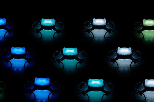 Multiple small drones illuminated with various colored lights, arranged in a grid pattern against a dark background